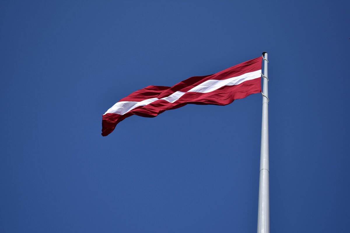 Die lettische Flagge — karminrot mit weißem Streifen — vor blauem Himmel.