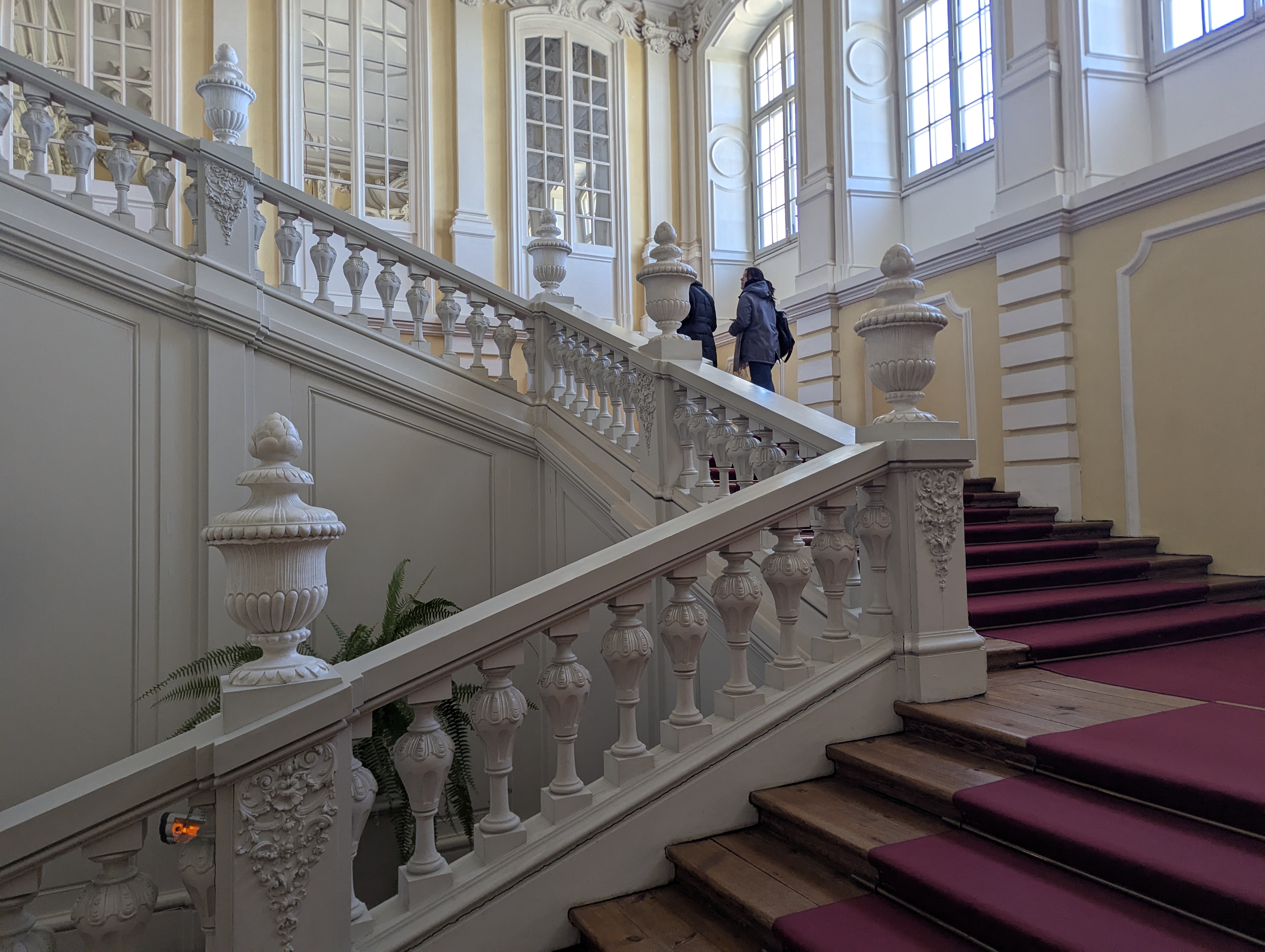Prachttreppe von Schloss Rundāle mit weißen Stuckbalustraden und burgunderrotem Teppich