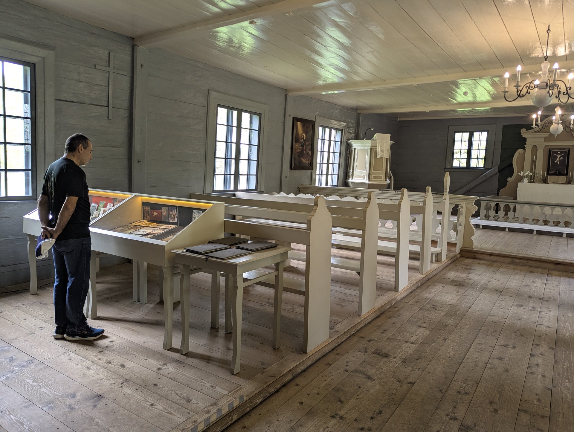 Innenraum einer hölzernen Vidzeme-Kirche mit Museumsexponaten und einem Besucher