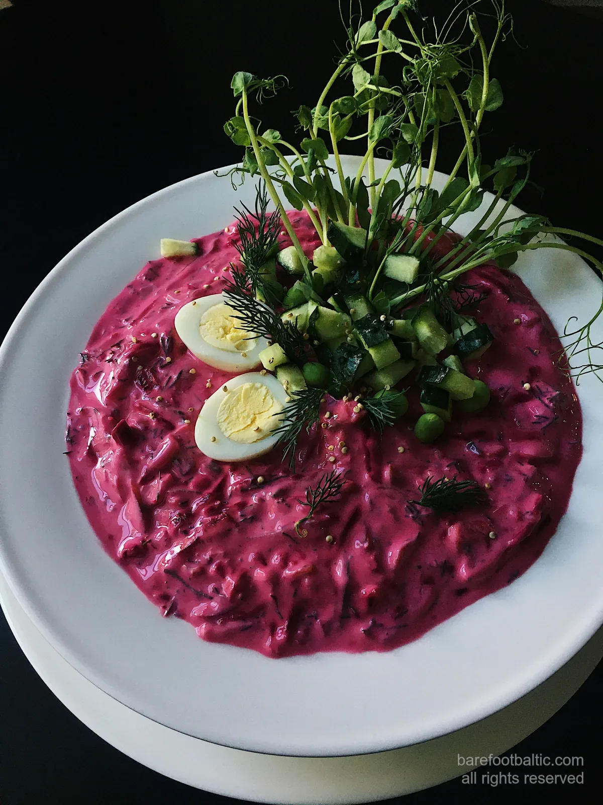 Eine Schale mit leuchtend rosa aukstā zupa, der lettischen kalten Sommersuppe aus Kefir und Rote Bete, garniert mit hartgekochtem Ei, Gurke und Dill