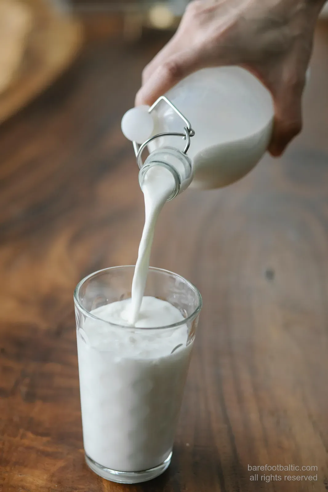Lettischer Kefir wird aus einer Flasche in ein Glas auf einem Holztisch gegossen
