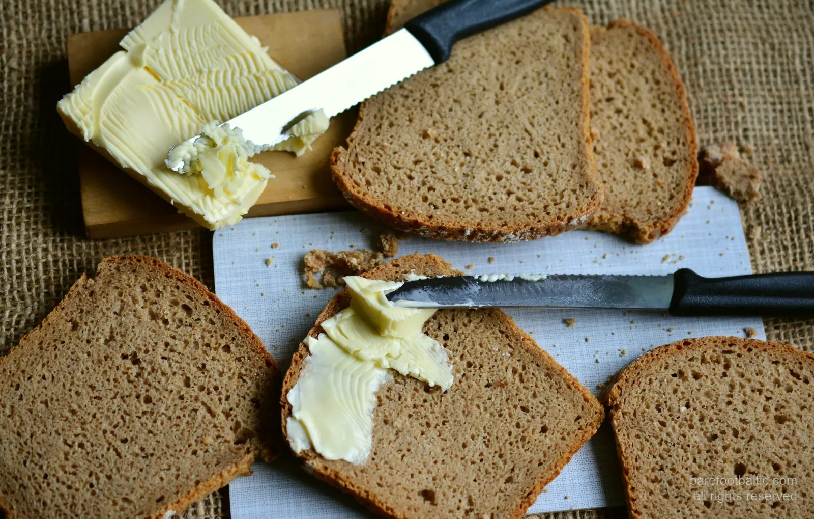 Scheiben von Rupjmaize-Roggenbrot mit Butter und einem Messer auf Leinen