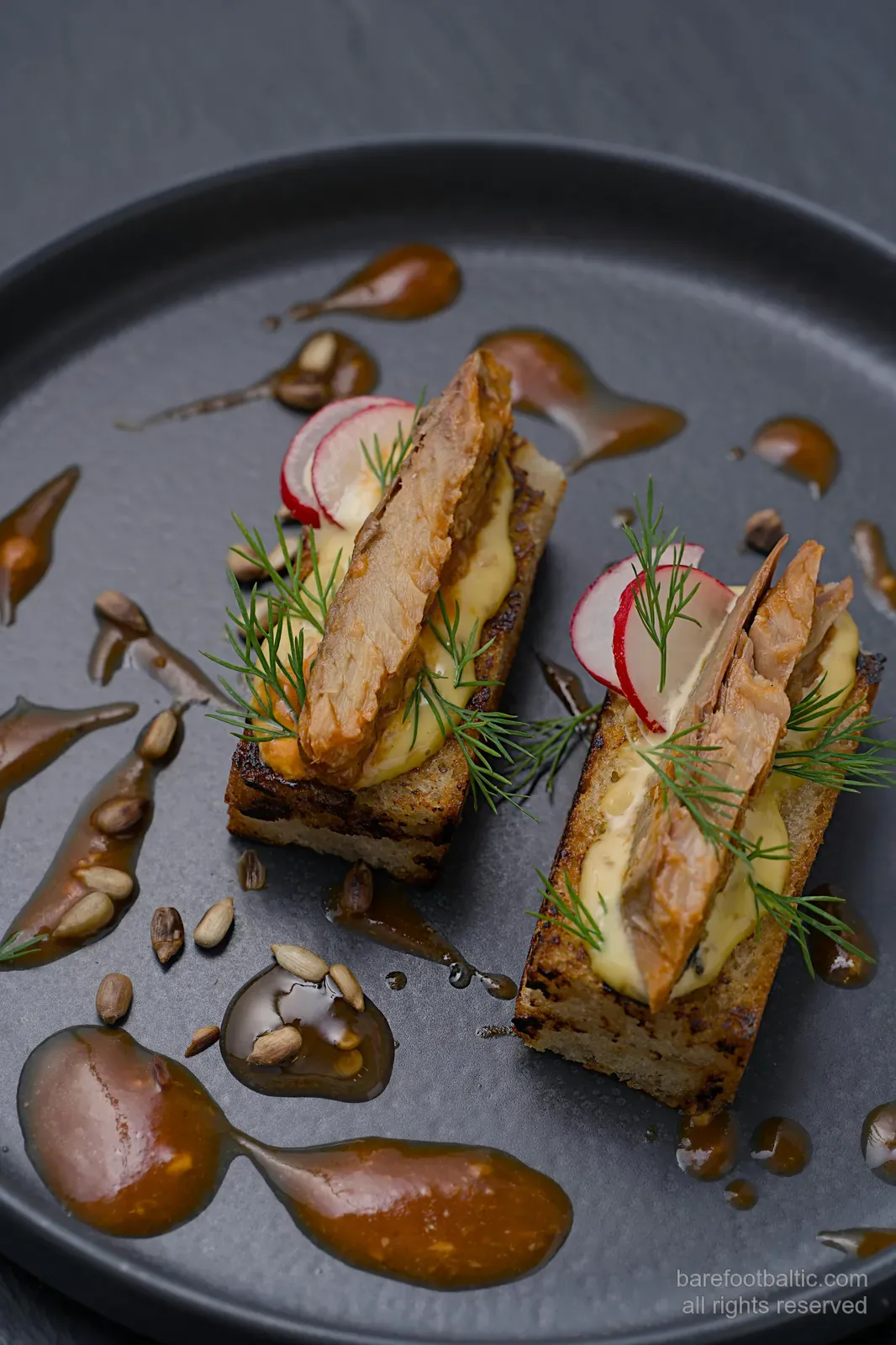Räucherfisch-Vorspeise auf getoastetem Roggen mit Sahne, Dill und Radieschen, auf einem schwarzen Teller serviert