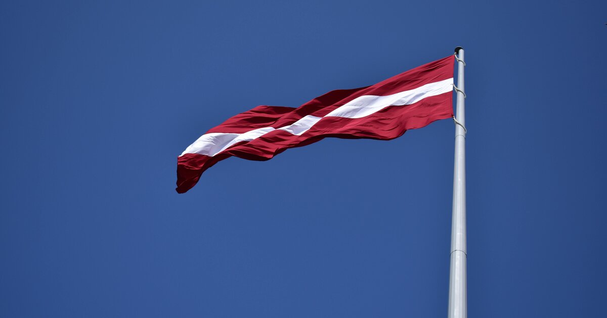 Die lettische Flagge — karminrot mit weißem Streifen — vor blauem Himmel.